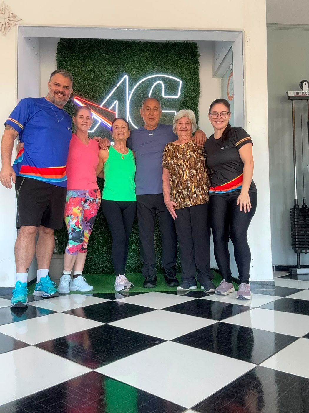 Grupo de alunos e professores do estúdio AC reunidos em frente ao letreiro da marca